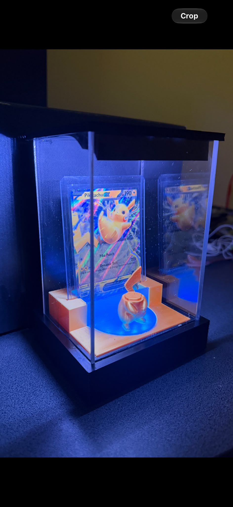 The Hololume case lit up in a dark room, with a card in a toploader and a figure on the glowing stage